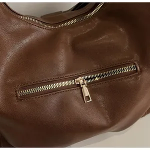 Detail view of the smooth golden metal zipper closure on a brown vintage leather tote bag