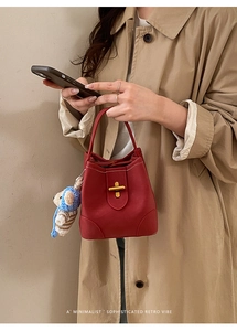 Close-up of red leather bucket bag with gold cross-bar lock and crochet bear charm