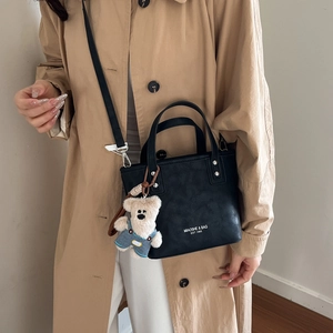 Detail of black leather bucket bag featuring white text logo and a cute plush bear charm