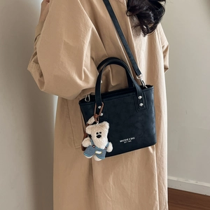 Model wearing a black leather bucket bag with white typography and a cute bear charm