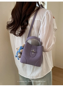 Detail of purple bucket bag with white stitching, metal lock, and blue bear charm