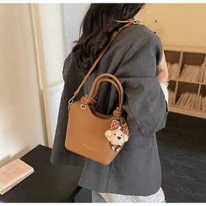 Brown litchi grain bucket bag with gold lettering and cute bear charm shown on model