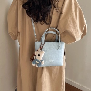 Close-up of light blue mini bucket bag featuring a cute teddy bear charm and brand logo