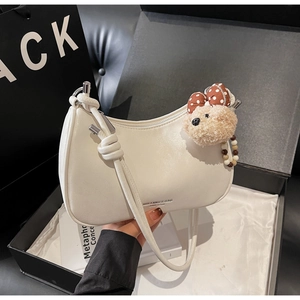 Detail of white half-moon shoulder bag with plush bear charm and delicate leather texture