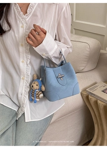 Close-up of a light blue bucket bag with a metal buckle and a cute puppy plush charm