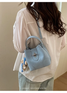 Light blue bucket bag with metal turn-lock and knit bear charm worn by a model
