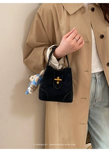Detail of black suede bucket bag with gold clasp and blue striped bear pendant