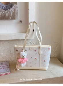 Detail of cream tote bag featuring pink cat print and a plush teddy bear charm