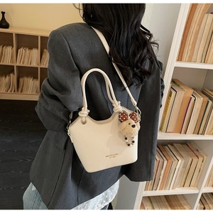 Detail of cream pebbled leather bucket bag with wave edge and cute teddy bear charm