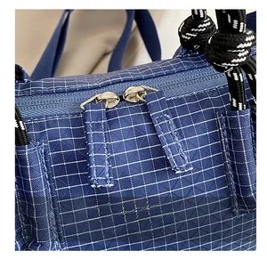 Detail showing smooth dual zippers and braided rope handle on blue plaid handbag