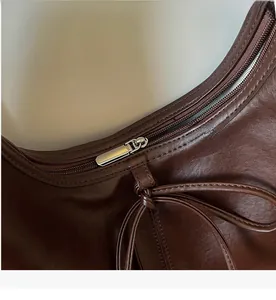 Detail of smooth silver zipper and leather texture on a dark brown bow tote bag