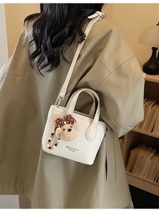 Chic beige bucket bag with bear pendant shown on model for casual commuting and crossbody use