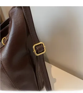 Detail of adjustable long shoulder strap with gold buckle on dark brown leather tote bag