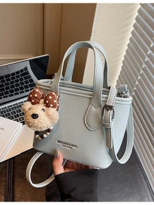 Light blue pebble leather bucket bag with top handles and a plush bear pendant charm