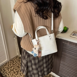 Detailed shot of a white matte leather bucket bag with a cute plush bear charm