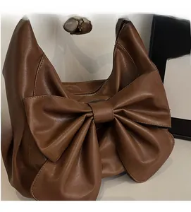 Close-up of brown leather tote bag featuring a large bow and white lace trim details