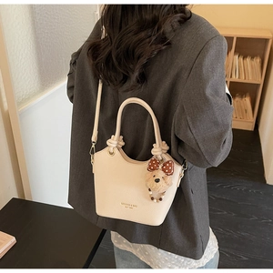 Detail of off-white lychee texture bucket bag with plush bear charm and bow detail