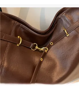 Detail of deep brown leather tote featuring glossy texture and gold metal hardware