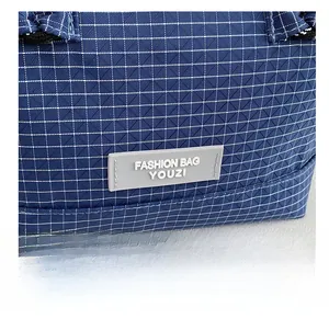 Close-up of dark blue plaid fabric texture with a silicone brand label on the handbag