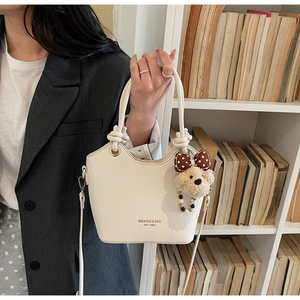 Detail of cream lychee leather bucket bag with plush bear charm and gold lettering