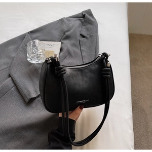 Detail of matte black dumpling bag featuring stylish knotted handle and silver brand logo