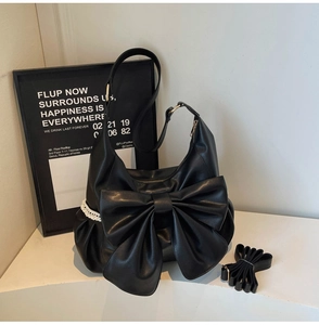Detail of black hobo bag showing leather bow, lace trim and adjustable shoulder strap