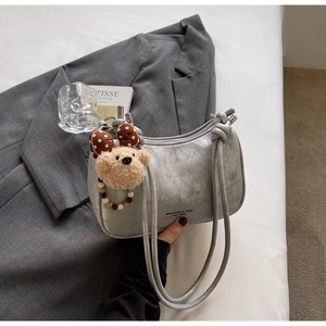 Detail of silver pleated leather bag with knotted strap and teddy bear charm accessory