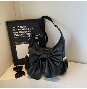 Close-up of black leather shoulder bag featuring a large bow and white lace side details