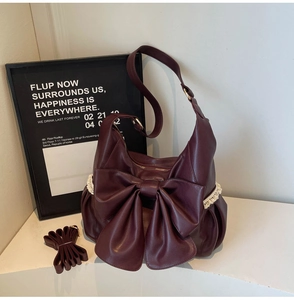 Detail of burgundy faux leather handbag with a large bow and delicate white lace trim