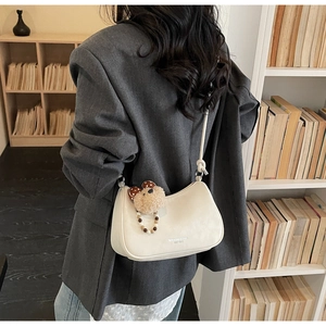 Detail of off-white dumpling bag with leather knot strap and plush bear charm accent