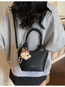 Minimalist black pebble leather bucket bag with teddy charm shown on shoulder
