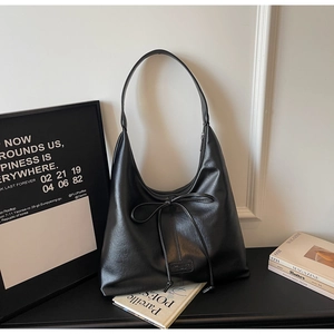 Detail of black faux leather hobo bag featuring a decorative leather bow and soft texture