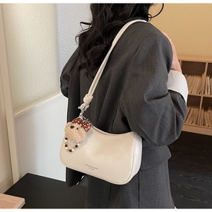 Side view of cream dumpling bag with cute teddy bear charm and soft strap detail