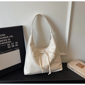 Close-up of cream PU leather half-moon shoulder bag with decorative bow drawstring detail