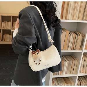 Detail of a beige dumpling-shaped shoulder bag with a cute plush bear charm