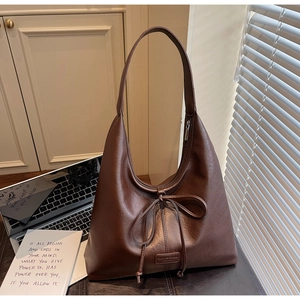 Detailed view of deep brown leather tote with drawstring bow and embossed logo plaque