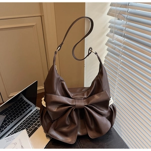 Detail of a brown shoulder bag featuring a large bow and delicate white lace trim