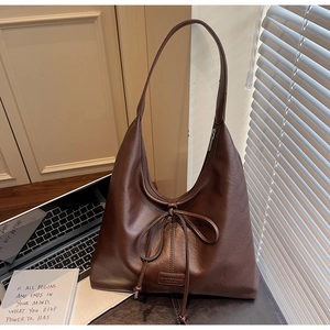 Close-up of brown faux leather tote bag showing fine texture and decorative bow detail