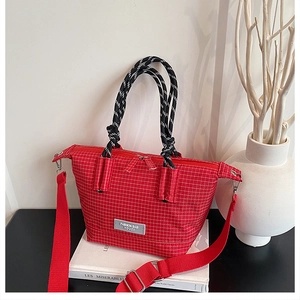 Detail of red checkered handbag featuring braided handles and wide crossbody strap