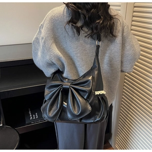 Detail of black hobo bag featuring a large bow and white lace trim on a model