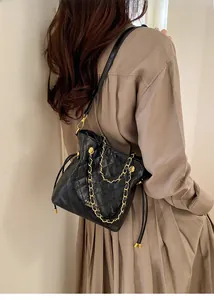 Detailed view of black quilted bucket bag with gold chain strap on a female model