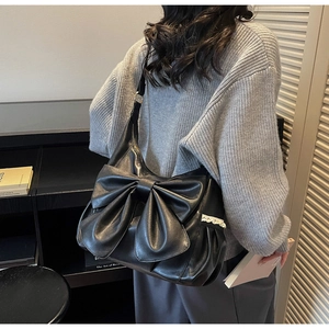 Detail of black bow shoulder bag with white lace trim and glossy PU leather finish