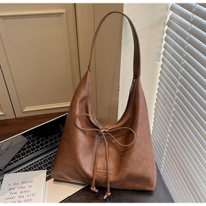 Detail of a brown leather tote bag with a decorative bow and embossed logo on the bottom