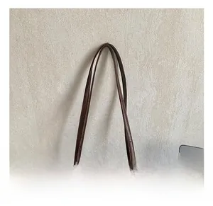 Detail of adjustable long handles on a brown matte leather shoulder bag with silver rivets