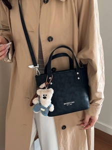 Minimalist black bucket bag with plush bear charm worn with khaki trench coat