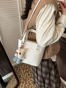 White bucket bag with cute bear charm worn as a crossbody bag in a vintage indoor setting