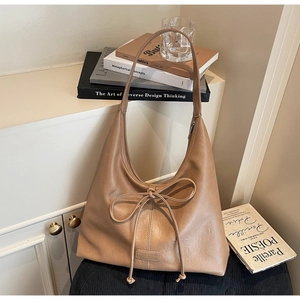 Detailed view of the brown leather tote bag featuring a bow tie and small metal logo