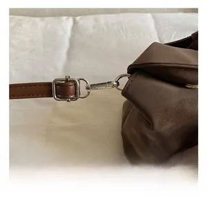 Detail of silver hardware hook and strap connection on brown matte leather bag