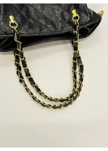 Close-up of black quilted bucket bag featuring a gold metal chain and leather handle