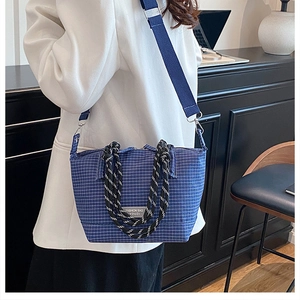 Detail of dark blue plaid crossbody bag with woven handles and fashion brand label